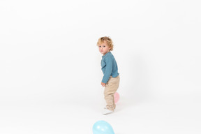 Baby boy standing among balloons and looking into camera