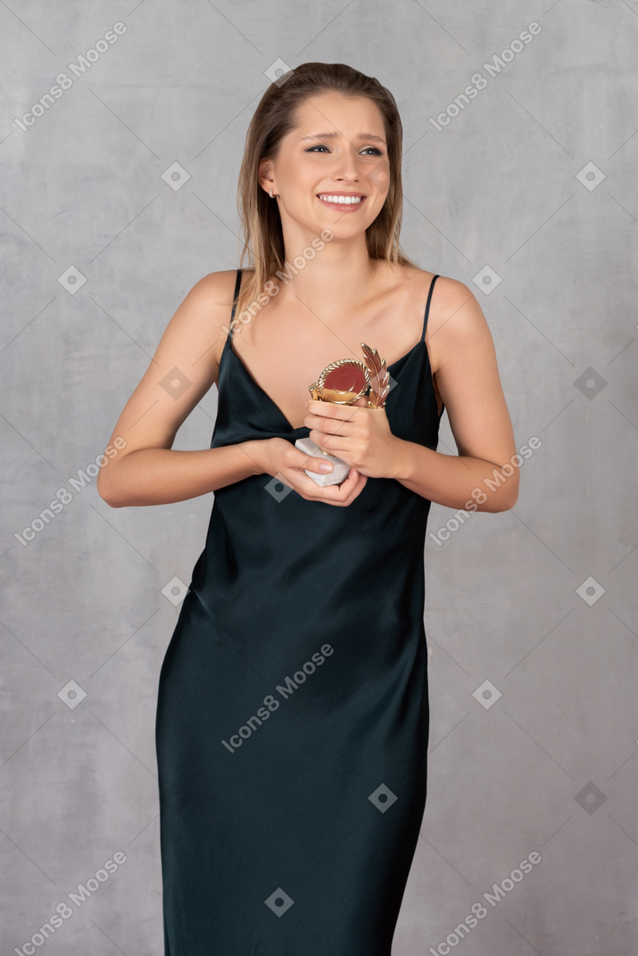 Front view of a happy young woman in night gown holding an award