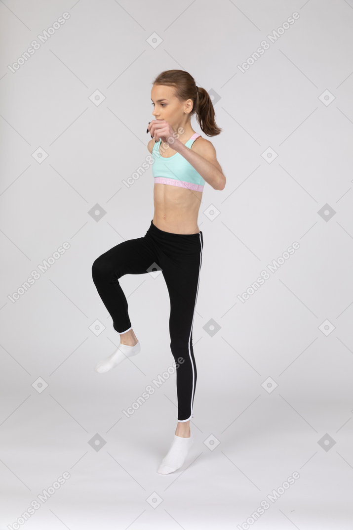Three-quarter view of a teen girl in sportswear raising hand and jumping