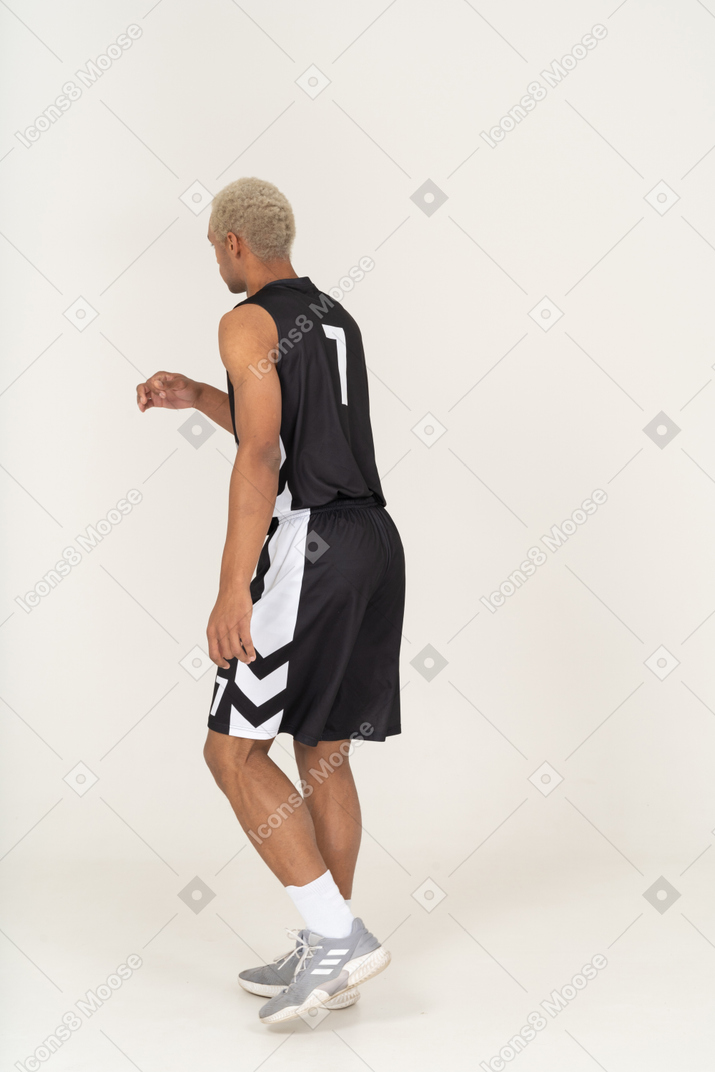 Three-quarter back view of a walking young male basketball player raising hand