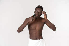 Um jovem negro com uma toalha de banho branca em volta da cintura fazendo sua rotina matinal