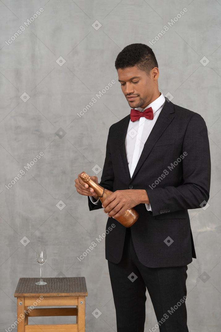 Young man looking down at a champagne bottle and opening it