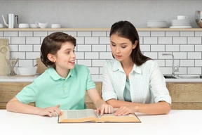 A woman and a boy sitting at a table reading a book