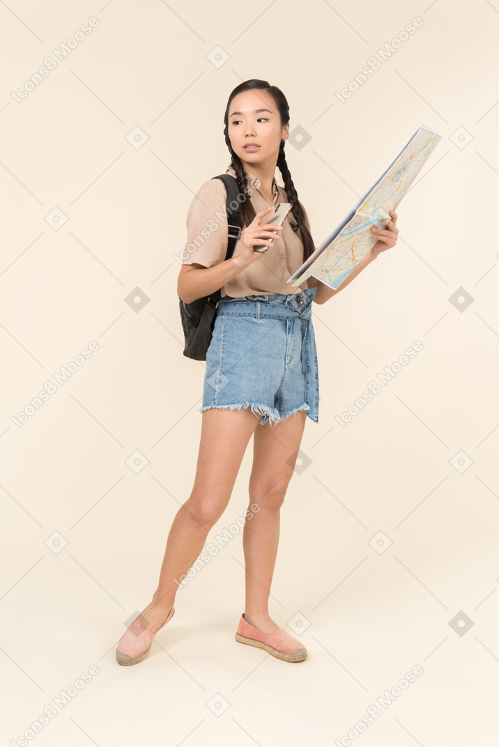 Young female traveller holding city map and smartphone in another hand