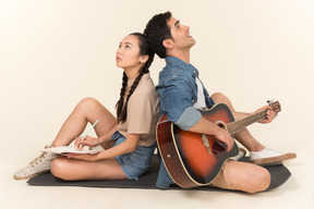 Rire interracial couple assis dos à dos et homme jouant de la guitare