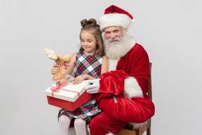 Garota garoto sentado nos joelhos do papai noel e segurando o brinquedo de pelúcia de veado