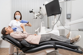 Longitud total de una dentista riendo sosteniendo un instrumento dental y una paciente en un gabinete de hospital