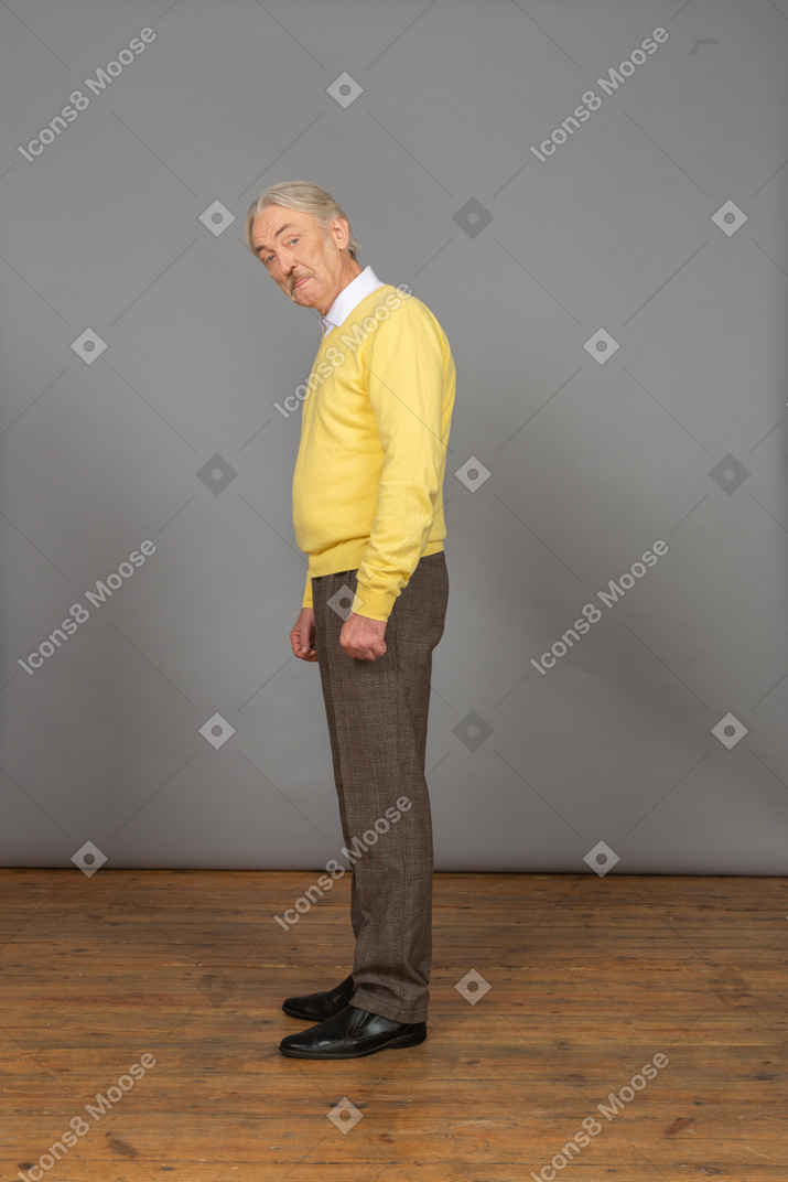 Vista lateral de um velho vestindo um pulôver amarelo e mostrando a língua enquanto olha para a câmera