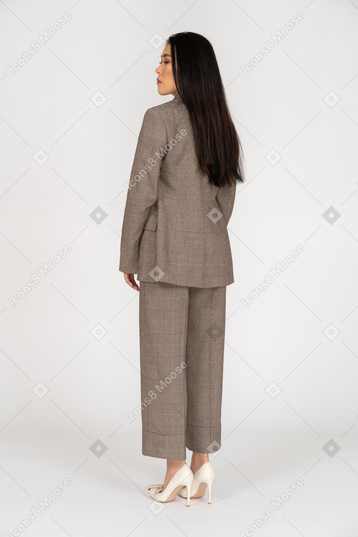 Вид сзади в три четверти молодой леди в коричневом деловом костюме, смотрящей вниз
