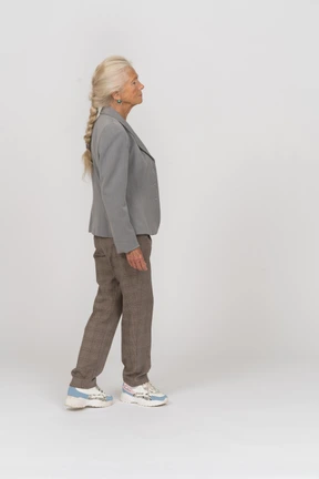 Side view of an old lady in suit standing with crossed legs