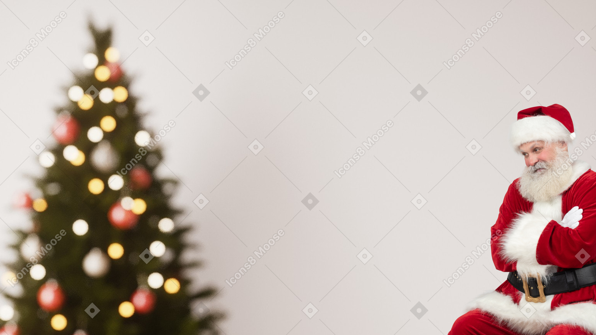 A man dressed as santa claus sitting in front of a christmas tree