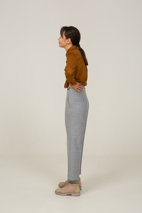 Vista laterale di una giovane donna asiatica in calzoni e camicetta che mette le mani sui fianchi