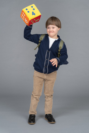 Little boy with a backpack holding up plush dice