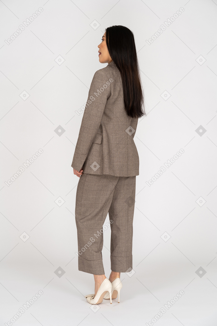Three-quarter back view of a young lady in brown business suit licking her lips