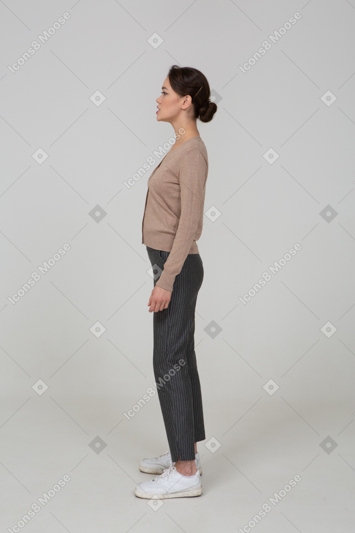 一位年轻女士站在套头衫和裤子放在一边看的侧视图