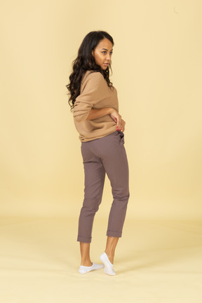 Three-quarter back view of a dark-skinned young female rolling up her pullover