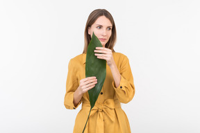 Joven mujer sosteniendo una hoja verde junto a su cara