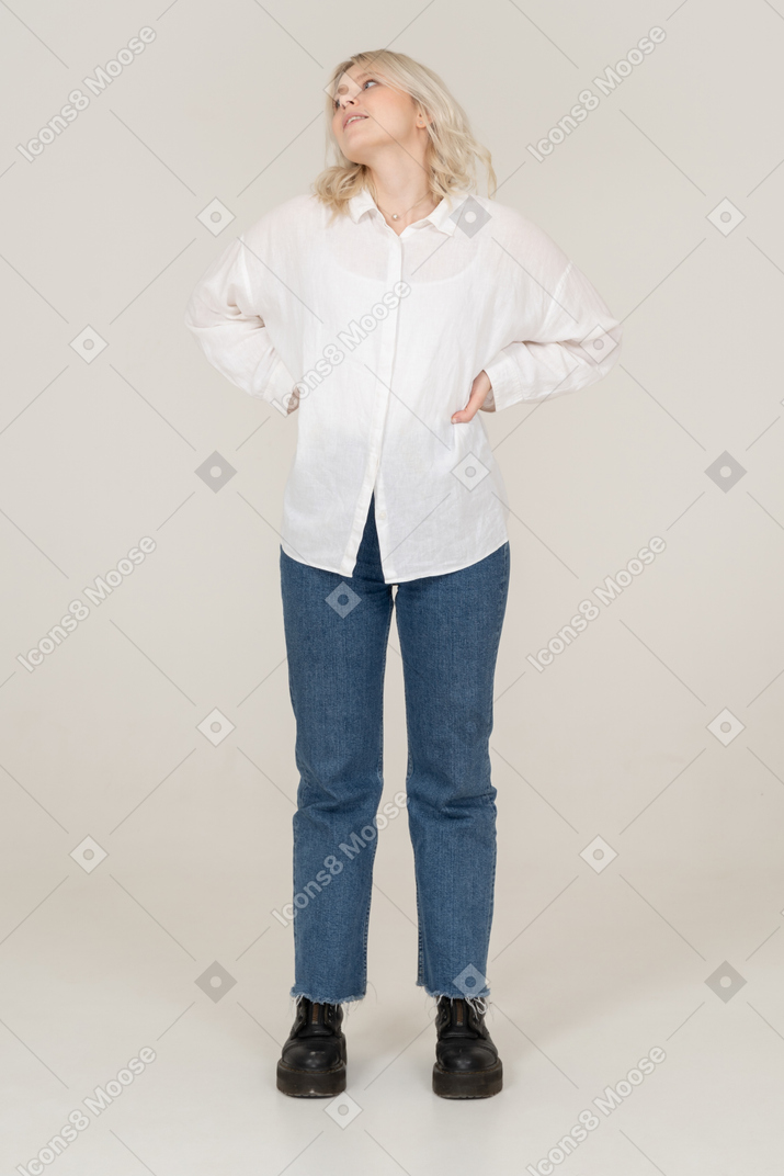 Front view of a blonde female in casual clothes putting hands on hips and looking up