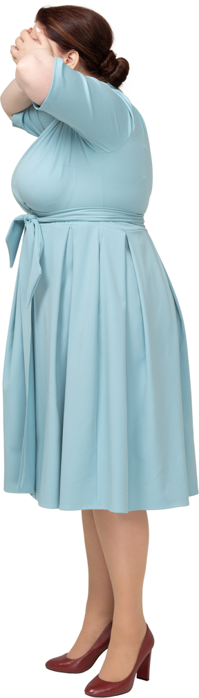 Vista lateral de una mujer en vestido azul que cubre los ojos con las manos