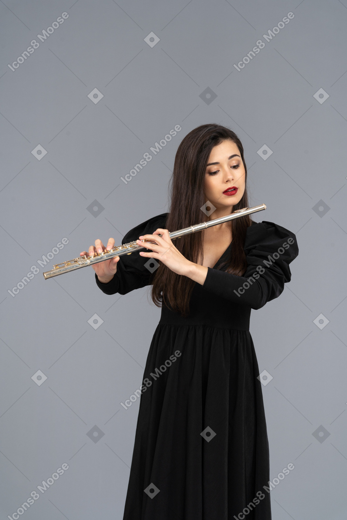 Vista frontal de uma jovem séria de vestido preto tocando flauta