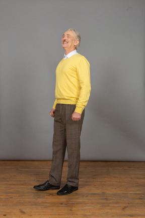 Three-quarter view of a smiling happy old man in a yellow pullover looking aside