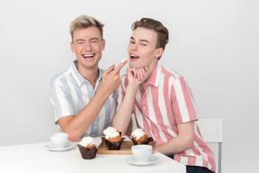 Man putting a finger with cupcake cream on it in his partner's mouth for him to lick