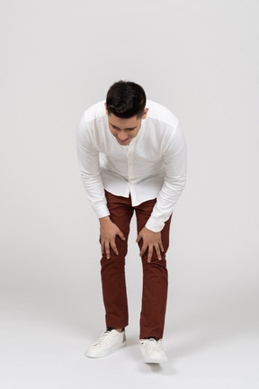 Front view of a young latino man leaning forward and resting his hands on his knees with a smile