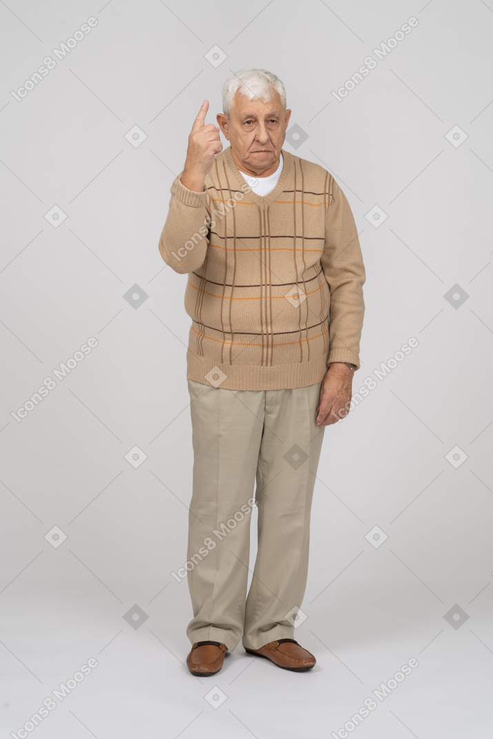 Vorderansicht eines alten mannes in freizeitkleidung, der mit dem finger nach oben zeigt