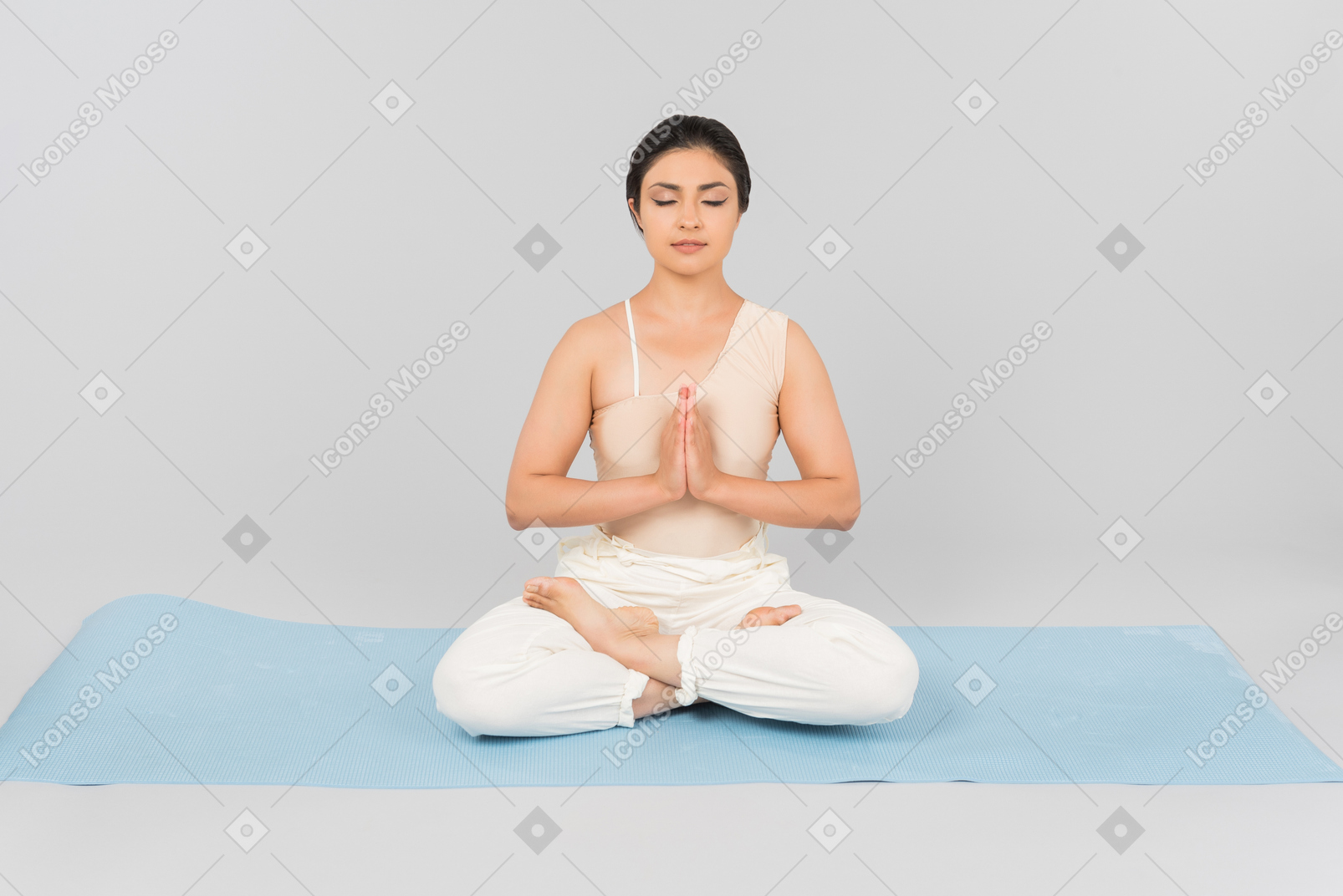 Junge indische frau sitzt auf yoga-matte mit gekreuzten beinen, gefalteten händen und geschlossenen augen