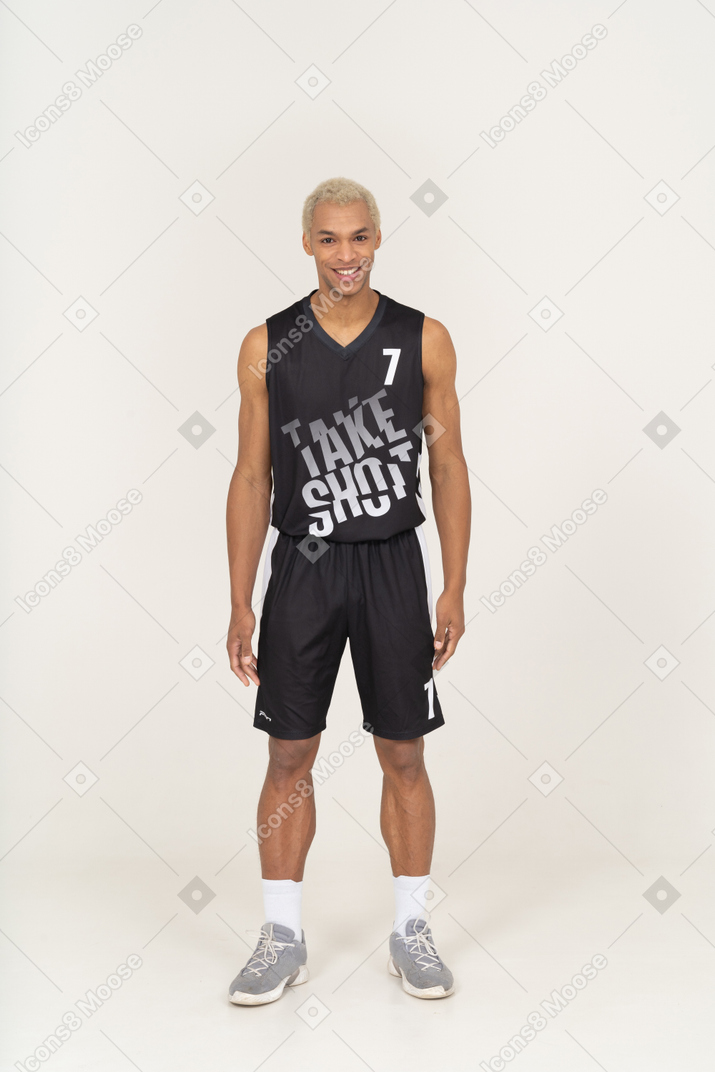 Vista frontal de un sonriente joven jugador de baloncesto de pie todavía