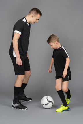 De cuerpo entero de un joven entrenando a un niño pequeño cómo jugar fooyball