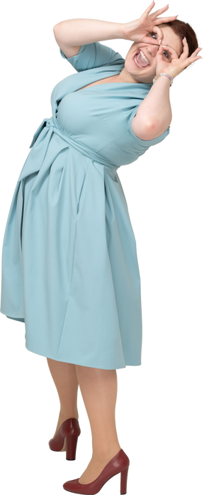 Вид сбоку на женщину в синем платье, смотрящую в воображаемый бинокль
