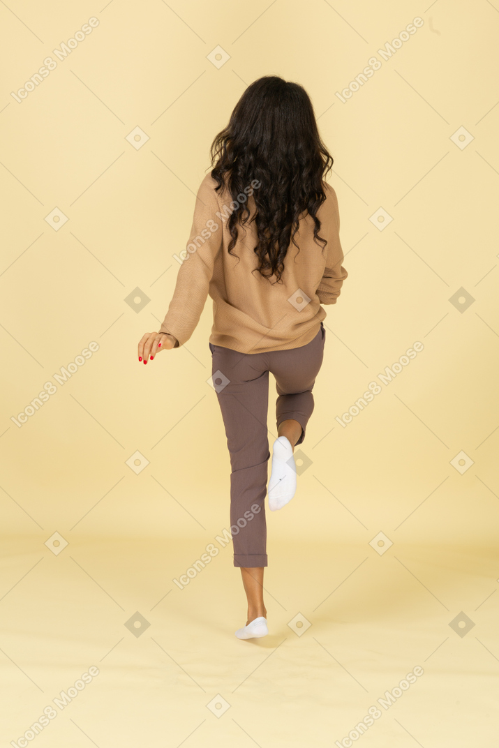 Vista posteriore di una giovane femmina dalla pelle scura in marcia alzando la gamba