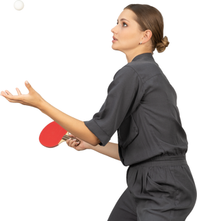 Vista lateral de uma jovem com um macacão servindo bola de tênis