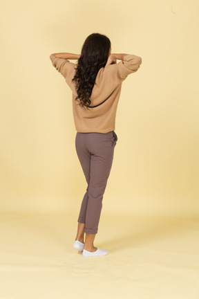 Three-quarter back view of a dark-skinned young female touching her shoulders