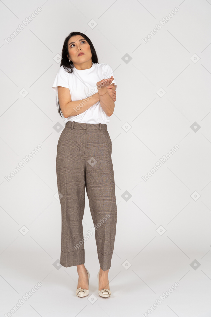 Vista frontal de uma jovem maravilhada de calça e camiseta levantando a mão