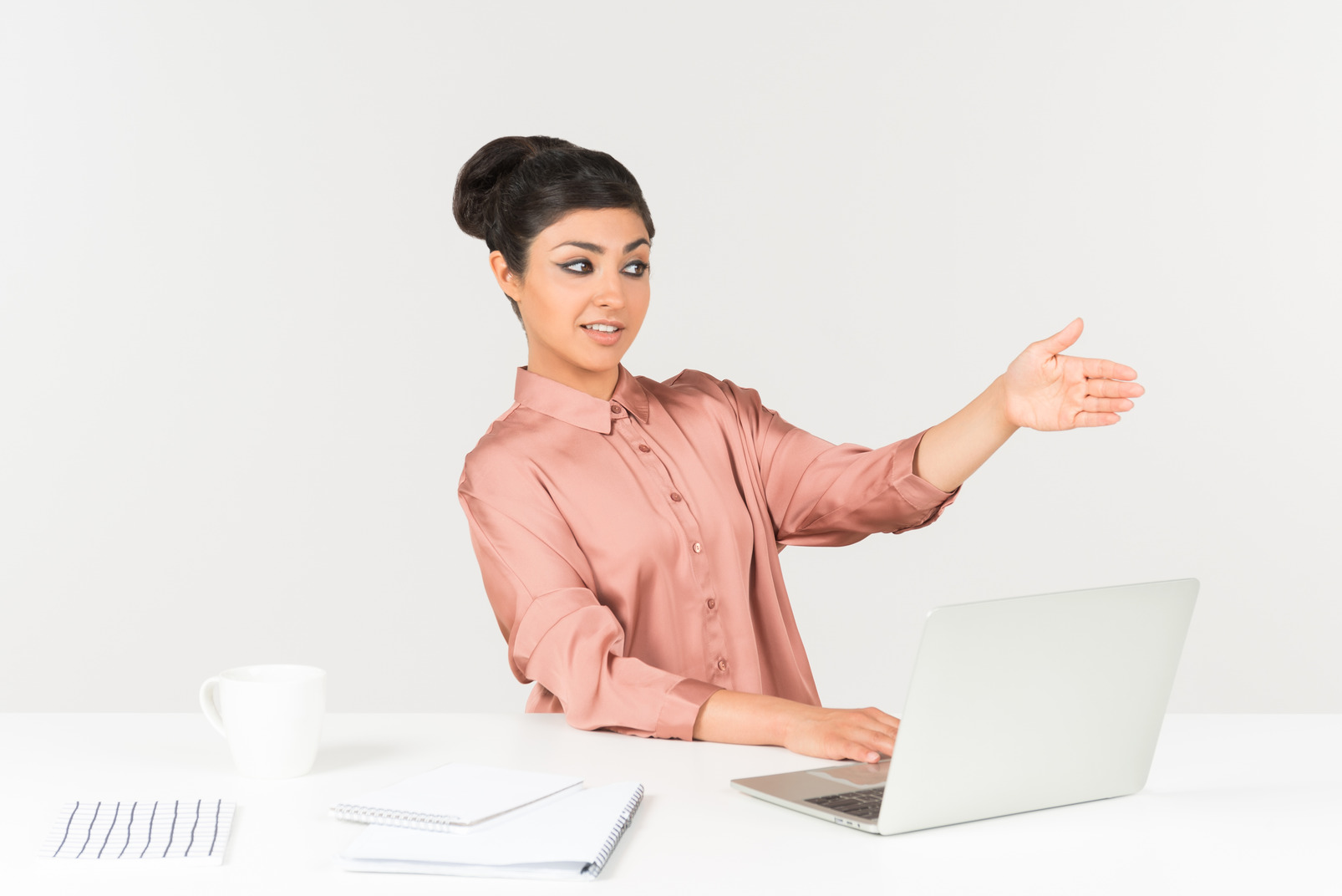 Young indian woman sitting at the office desk and pointing with a hand