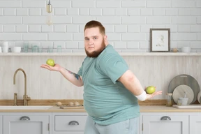 A fat man holding two apples in the kitchen