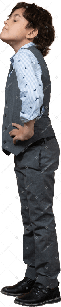 Side view of a cute boy in grey suit posing with hands on hips