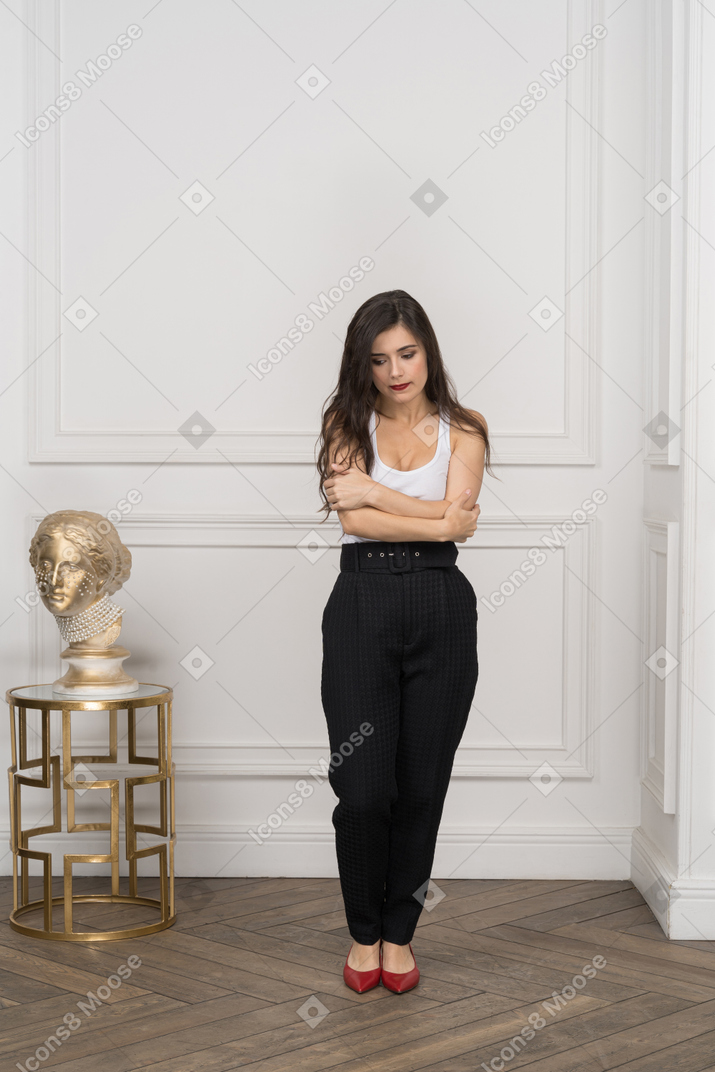 Full-length of a shy young female crossing hands while standing near golden greek sculpture