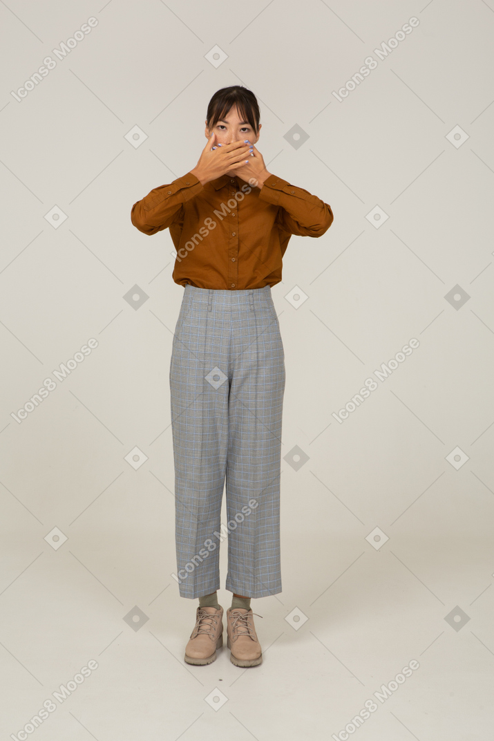 Vista frontal de una joven mujer asiática en calzones y blusa escondiendo la boca