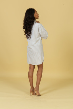 Vista posterior de tres cuartos de una mujer joven de piel oscura con vestido blanco ajustando su cuello