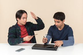 Due giovani geek sorridenti che si siedono alla tavola e che riparano computer portatile