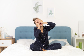 Вид спереди зевающей молодой женщины в пижаме, лежащей в постели и скрывающей лицо