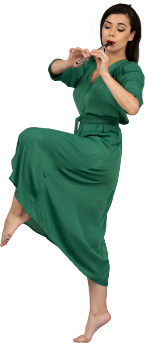 Vista laterale di una giovane donna che balla in abito verde, suonare il flauto
