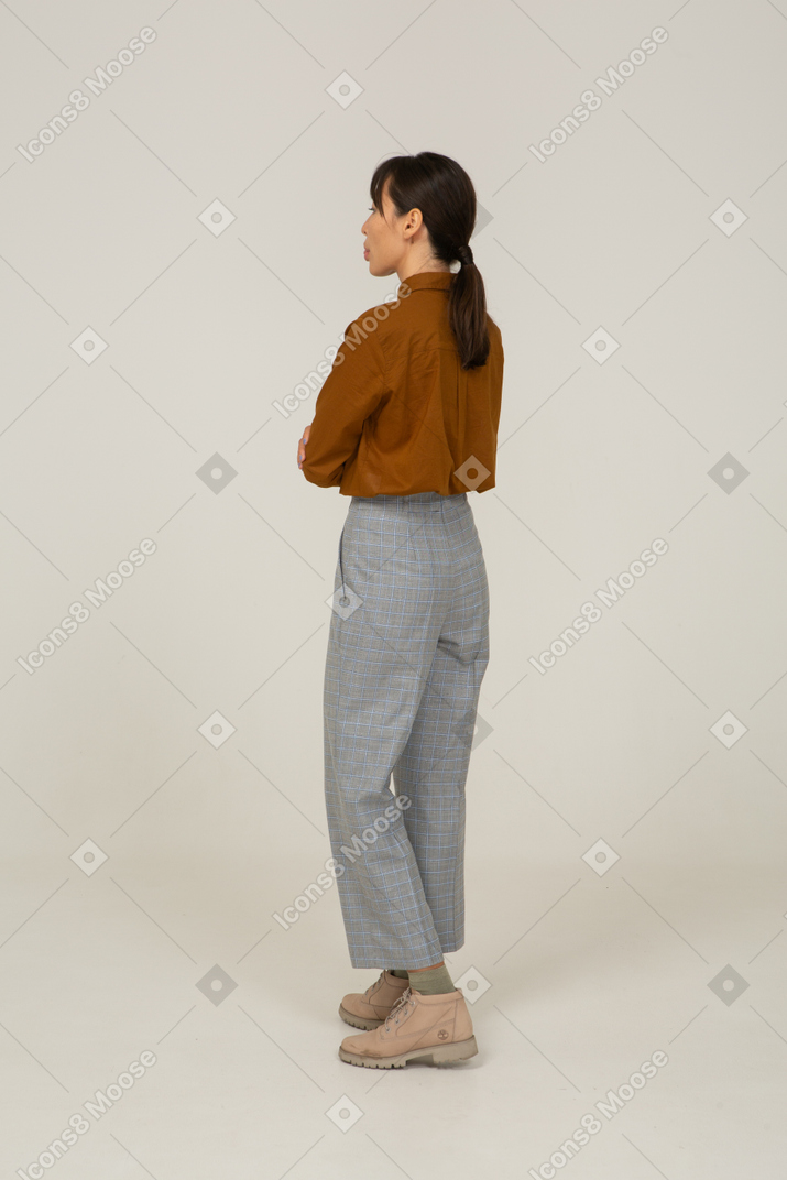 一位身着马裤和衬衫的年轻亚洲女性双臂交叉并露出舌头的四分之三后视图