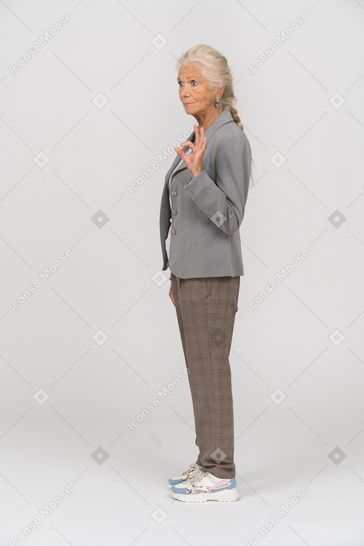 Vista lateral de una anciana en traje mostrando signo ok