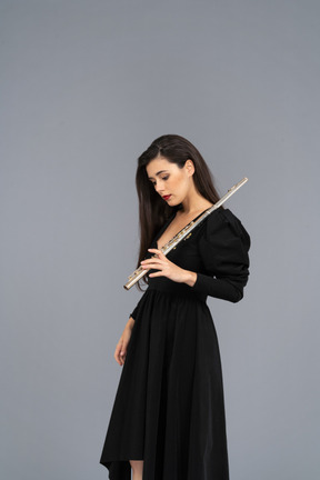 Vista de tres cuartos de una joven seria en vestido negro sosteniendo la flauta y mirando hacia abajo