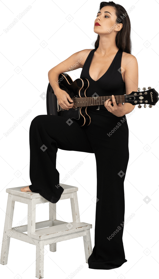 Dreiviertelansicht einer jungen dame im schwarzen anzug, die die gitarre hält und das bein auf den hocker legt
