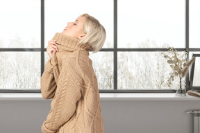 Woman in a warm sweater standing near the window